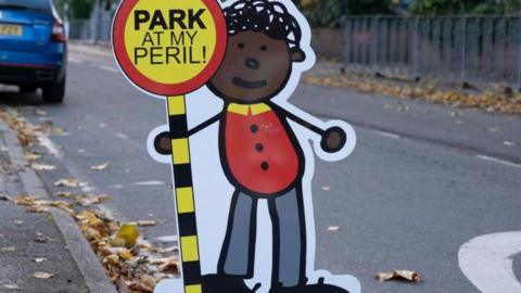 A cardboard cut out of a child holding a sign saying 'park at my peril'