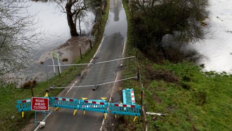 A 'road closed ahead' sign and green barriers block a road flooded with high waters on either side of it near to Harbridge in Hampshire, taken on Friday.