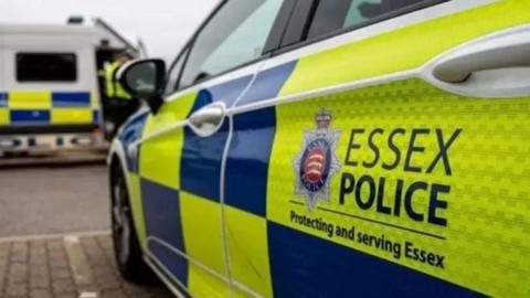 A Essex Police car parked in a bay. There is a police van driving in front.