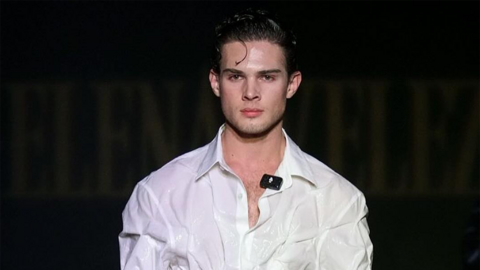 Clavicular in a white shirt on a runway. He has dark hair.