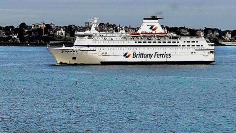 A Brittany Ferries ship at sea, with some land behind.