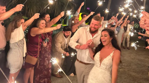 Family handout of Aric Hutchinson and Samantha Miller surrounded by guests during their wedding