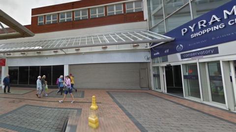 Shoppers walking in and out of the entrance to Pyramids Shopping Centre in Birkenhead some with shopping bags