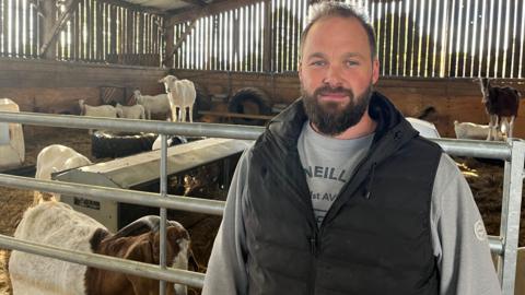 Matt standing in a barn in front of goats