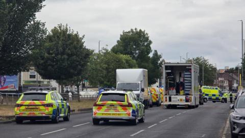 A number of police vehicles close off dual carriageway in Merseyside. The road has trees lined down the middle
