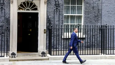 Starmer gestures with right hand while speaking in front of two microphones