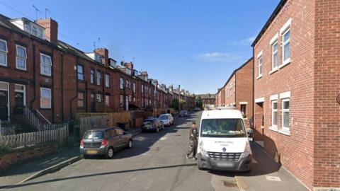 A terraced street showing cars on each side and blue sky 