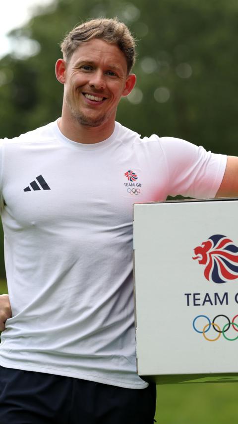 A man in a tight white Team GB shirt standing next to a box which has the Team GB logo on it.