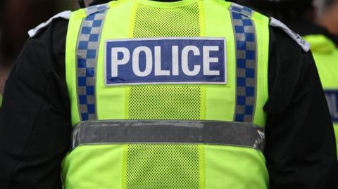 The back of a police officer in a hi-vis police vest, with the word POLICE stitched into the back.