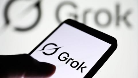 Grok logo displayed on a smartphone, with it's logo shown on a blurred, larger backdrop behind it. 