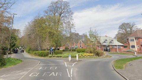 A big roundabout with trees and bushes in the middle of it with houses around the outside