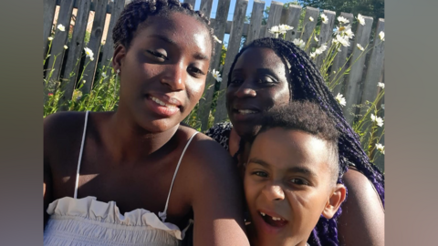 Naz Brightly has cornrows and is wearing a white strappy top. She is standing next to her mother Yvette and her brother Sammy.