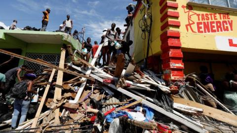 Men stand atop rubble beside a brightly-painted building