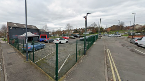 Cars behind a fence with a two-storey building in the background