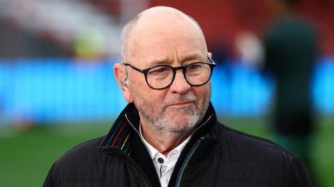 Gary Johnson standing on the pitch during a television broadcast for a match