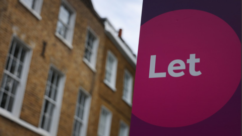 A pink and purple "Let" sign is in the foreground with a yellow brick property in the background.