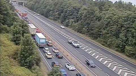 The A14, showing cars queuing on one side of the road, and cars driving on the other side. There are trees either side of the road. 