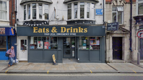 The front of Eats & Drinks in Weymouth, a convenience store with a sign that says "Eats & Drinks, your local convenience store"