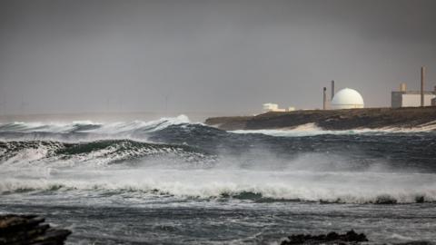 A view of the Dounreay nuclear power over waves crashing on the shore below. Dounreay is made up of a number of buildings, including its distinctive "golf ball", a spherical structure housing a nuclear reactor.