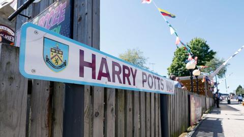 Close-up view of the claret and blue Harry Potts Way street sign in Burnley.