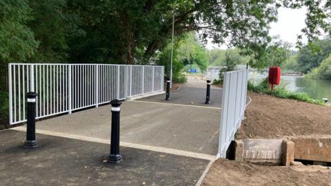 A new bridge, which is clearly wider, with cleaner rails and two bollards on either side of it - with the River Thames in the background of the picture 