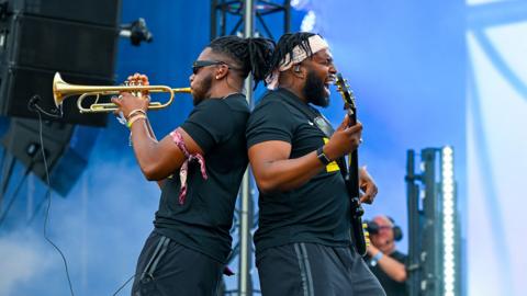 A man playing trumpet and a man playing bass guitar from Ezra Collective.