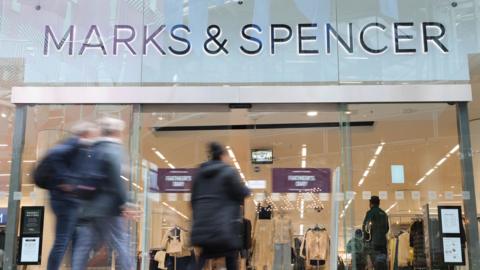 A Marks and Spencer store front with people walking inside its front doors.