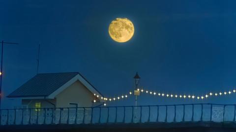 The Moon appears full in the night sky above a hut on Penarth Pier in Wales