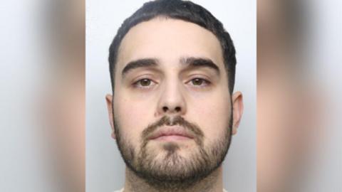 Police custody image of Adam Moore-Lynch with black hair and beard.