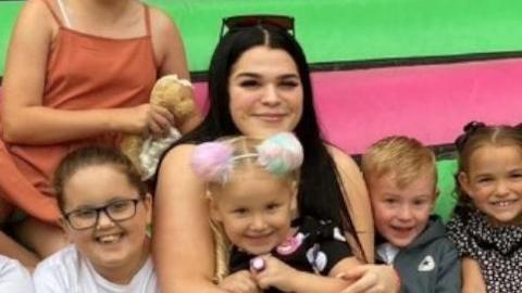 Alliyah Bell sat on a bouncy castle with several beaming children. She is smiling at the camera and has sunglasses atop her long black hair