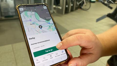 A close-up of the new app being used on a mobile at a train station