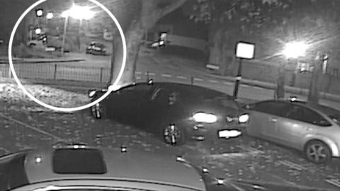 Grainy CCTV footage showing three cars in a car park and a white circle denoting where a firework attack took place at a house