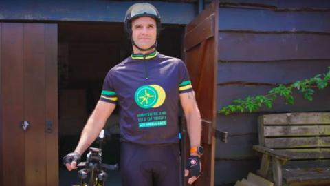 Michael Oakes wheeling his bicycle from his shed. He is wearing air ambulance-branded cycling gear