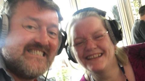 Guy Garvey and Beckie Garvey working on radio 10 years ago, both are wearing radio headphones and smiling into the camera