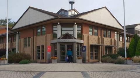 The Avon and Somerset Police headquarters building from the outside. It is a brick building and there are bushes around the entrance.