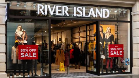A River Island shop front, with red "50% off sale" signs in the windows.