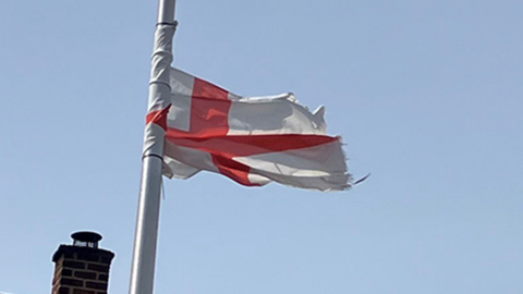 A St George's flag on a lamppost. In the background is the roof of a house with a solar panel on it
