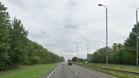 A two-laned road with traffic lights in the central reservation