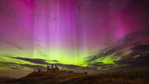 Pink and yellow colours from the Northern Lights visible in the night sky above a historic building 