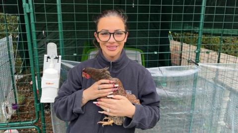 Katriona Shovlin holds a brown chicken outside a hen house at her home in Upchurch