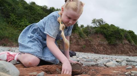 Tegan yn edrych ar ôl-troed dinosor ar draeth yn ne Cymru