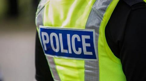 The back of a police uniform - a luminous vest with the world 'police' emblazoned across it