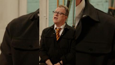 Russell T Davis is wearing glasses, an orange tie and a black jacket