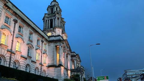 Stockport town hall, as taken from below and at night, when the windows are lit from underneath. It is a large white stone building.