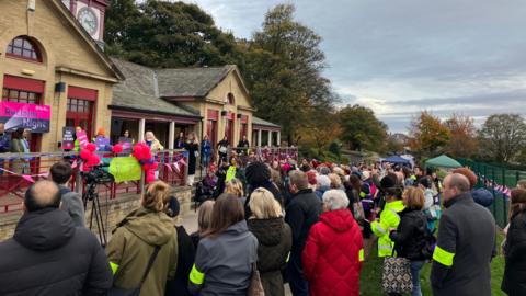 About 200 men and women gather outside a park building where mayor Tracy Brabin gives a speech