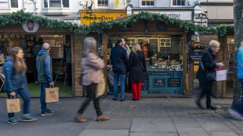 People walk past wooden chalet-style buildings selling a range of Christmas gifts, at York Christmas Market.