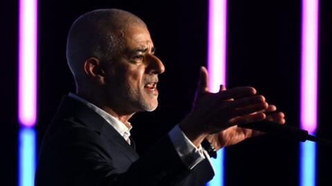 Mayor of London Sir Sadiq Khan delivers a speech during London Tech Week. He is pictured speaking into a microphone with his hands open either side of the microphone.