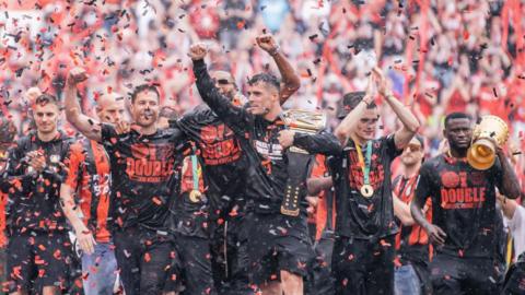 Bayer Leverkusen players celebrate with the league and cup trophies at the end of last season