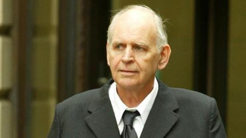 Tam Paton leaving court in 2006. He has white hair and is wearing a black suit and tie over a white shirt.