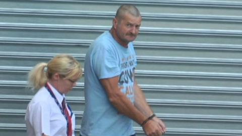 Gene Charles Bristow in handcuffs is escorted by a guard to Adelaide's District Court